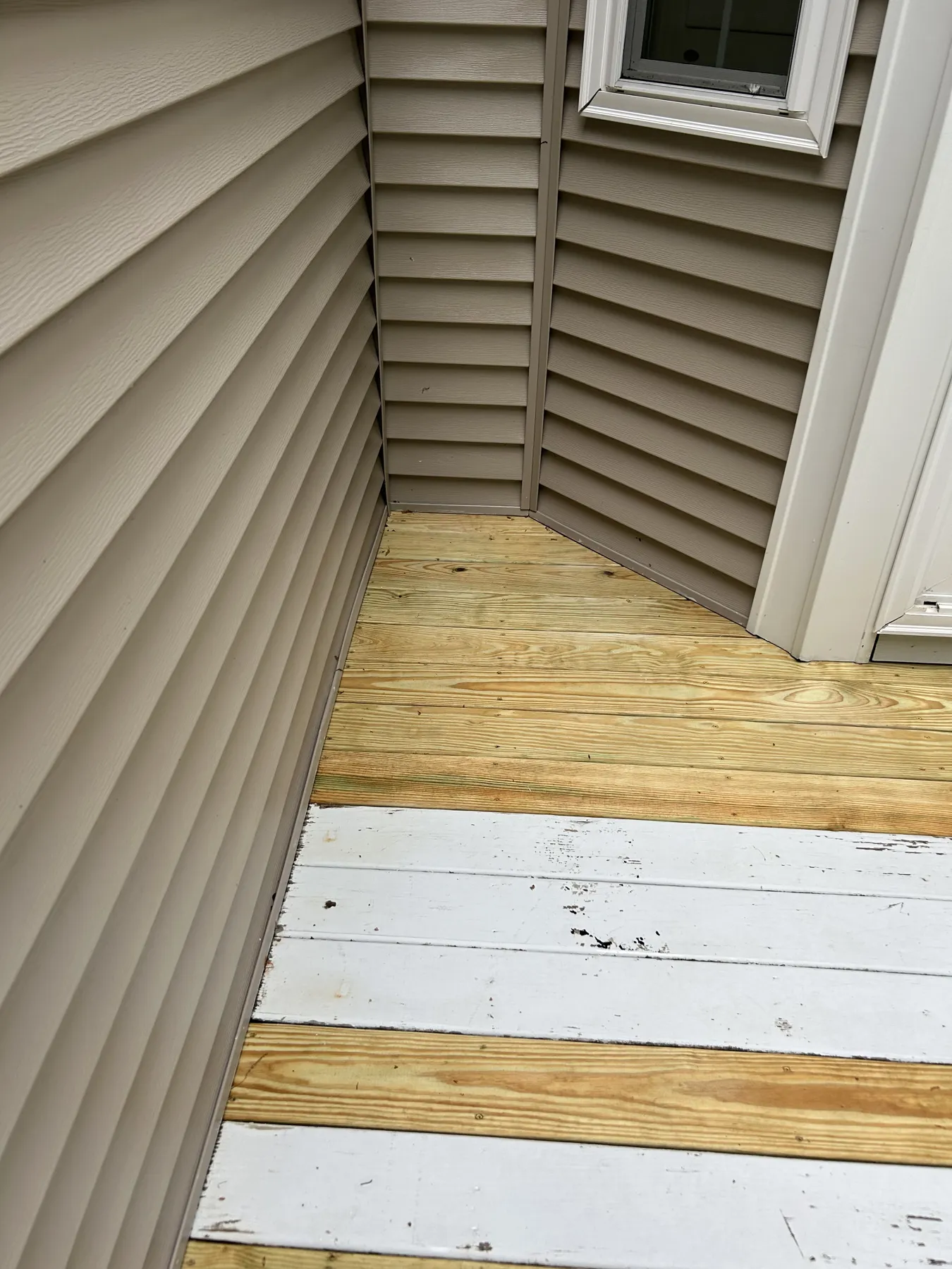 Freshly washed deck boards meeting tan vinyl siding at an inside corner