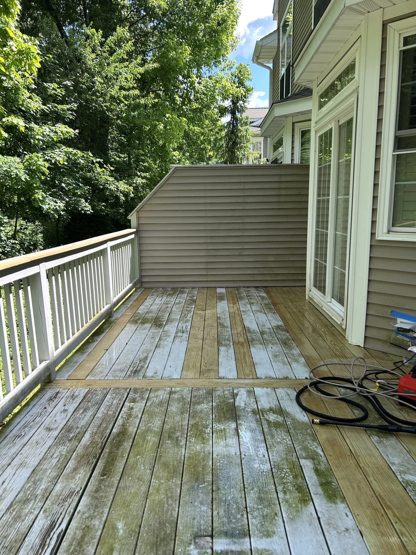 Before: a backyard deck with weathered boards, green with moss, beside tan vinyl siding