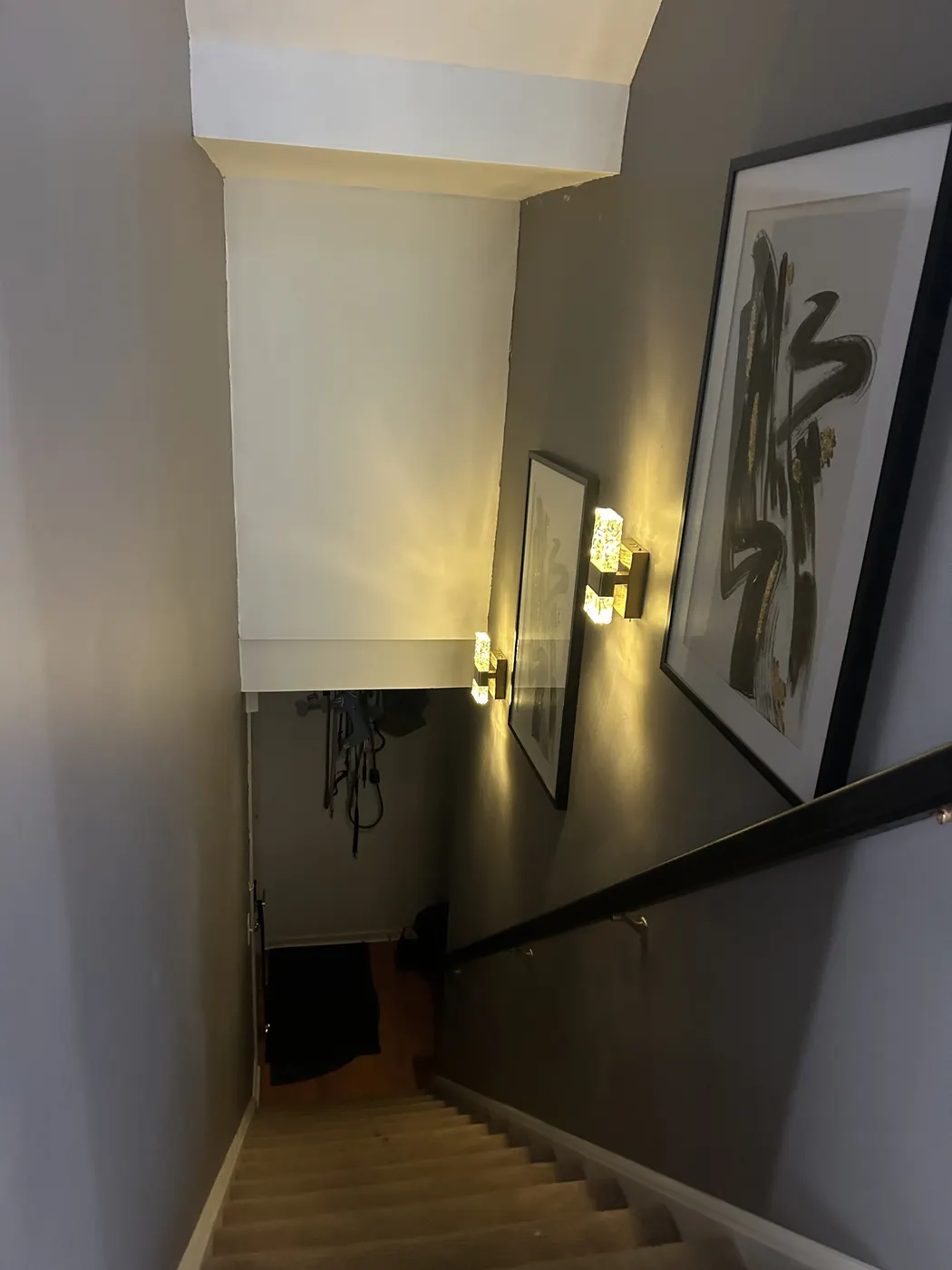 Finished stairwell with dark gray walls, framed art and gold wall lights