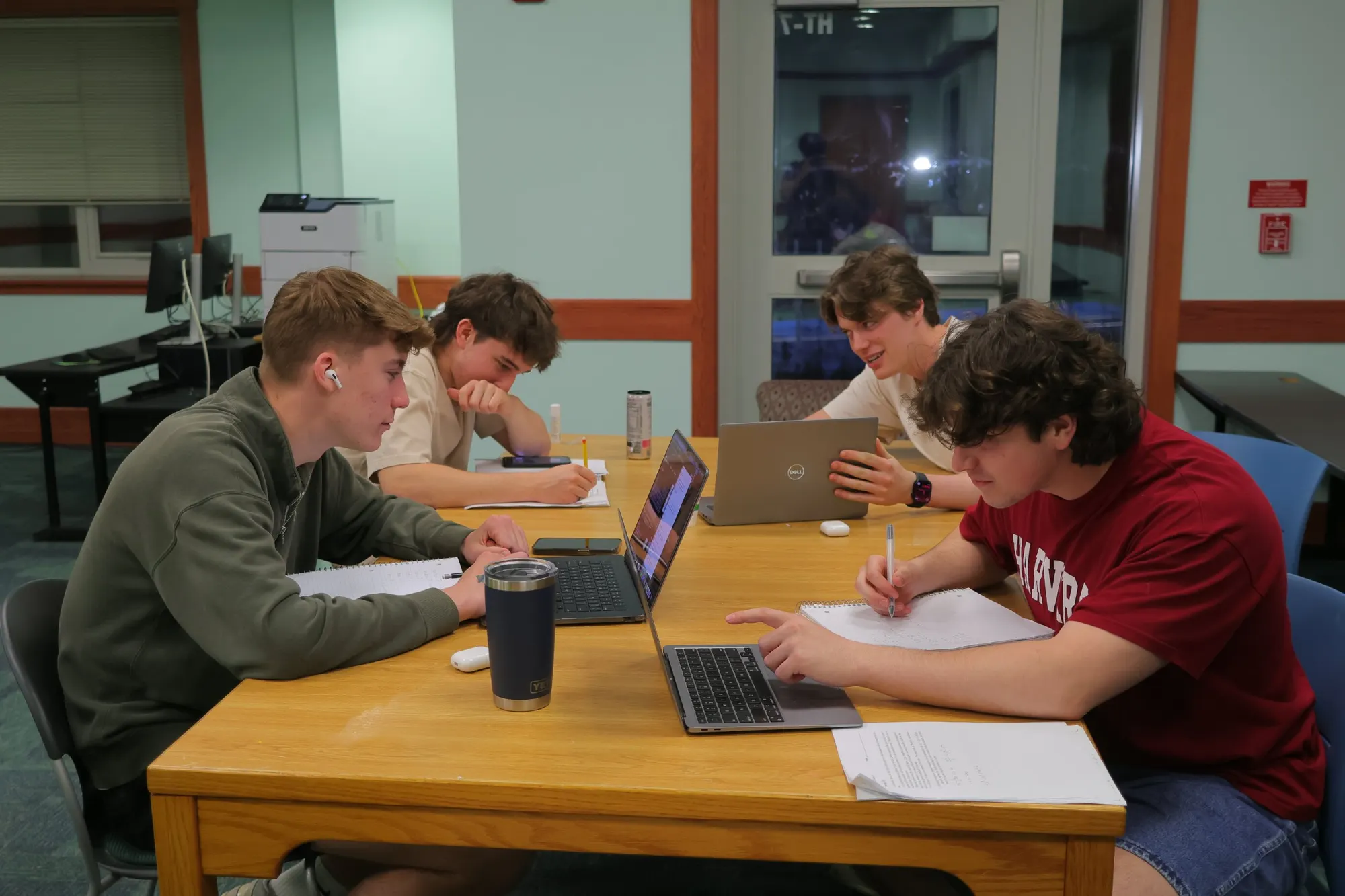 Four students around a library table with laptops and notebooks, working through problems together