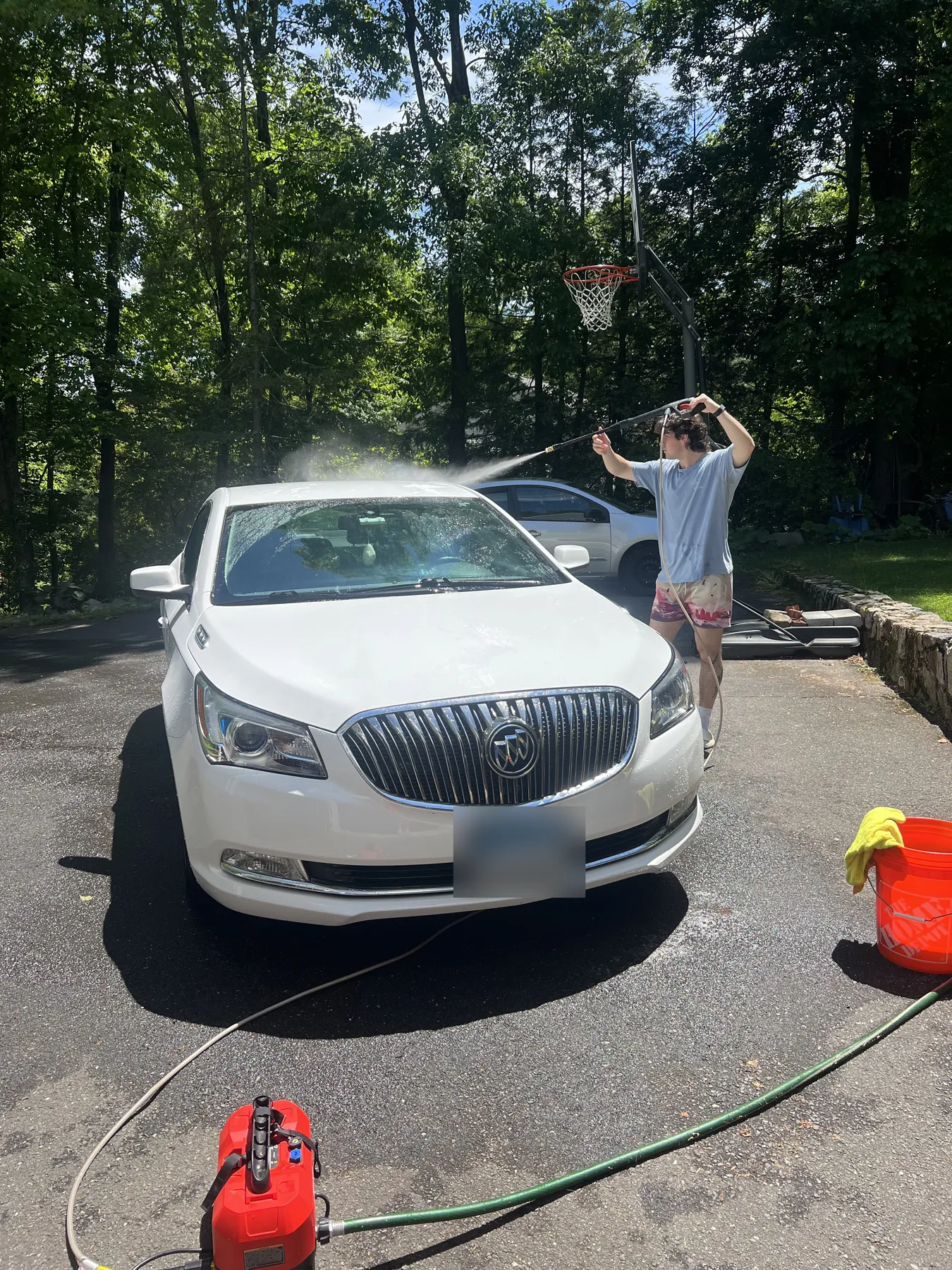 Evan pressure washing a white sedan in a driveway, spray arcing over the roof